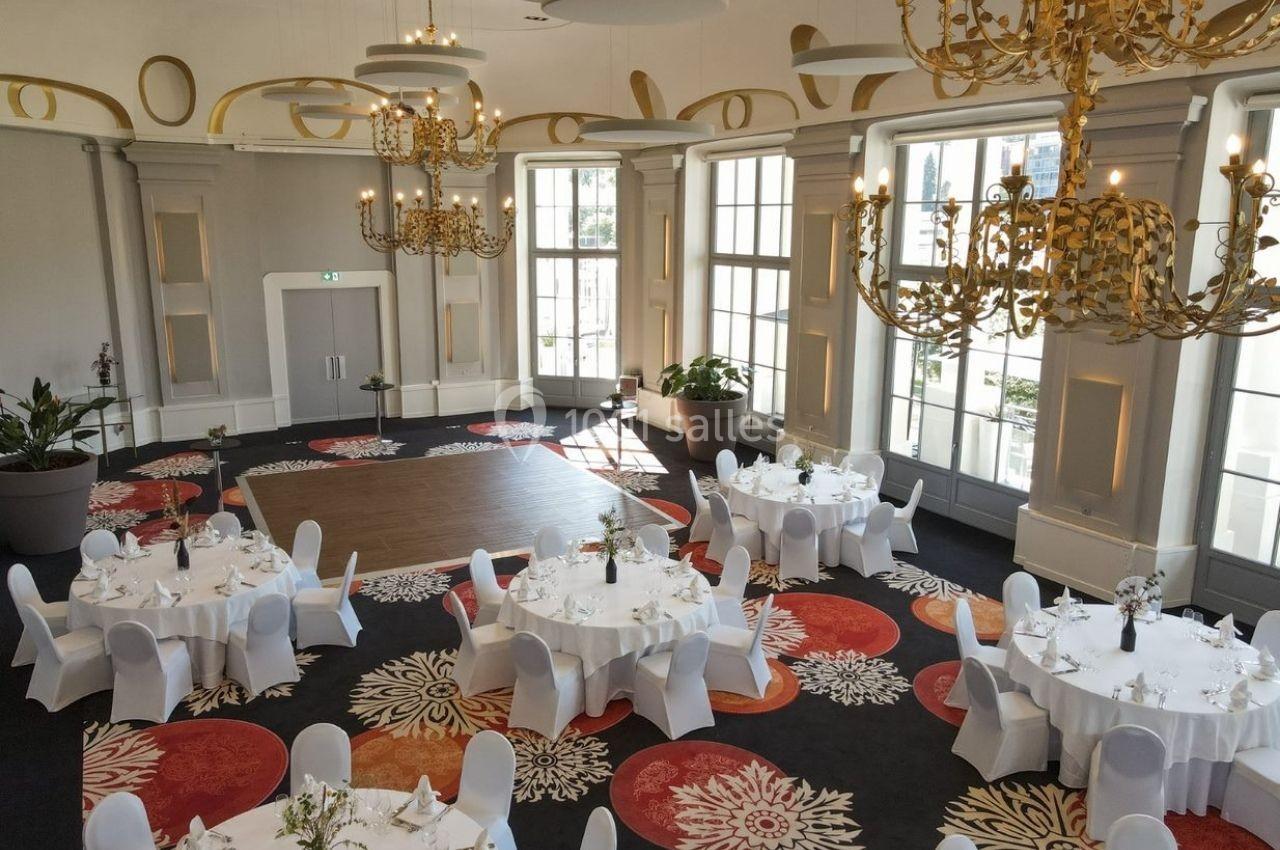 Salle de réception élégante avec tables rondes dressées, chandeliers dorés et grande piste de danse centrale.
