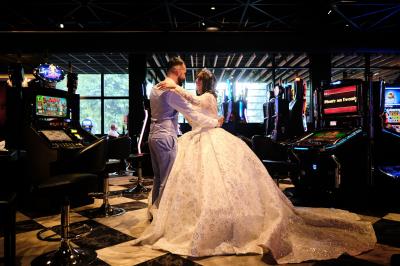 Un couple en tenue de mariage danse au milieu d'une salle de casino entourée de machines à sous.