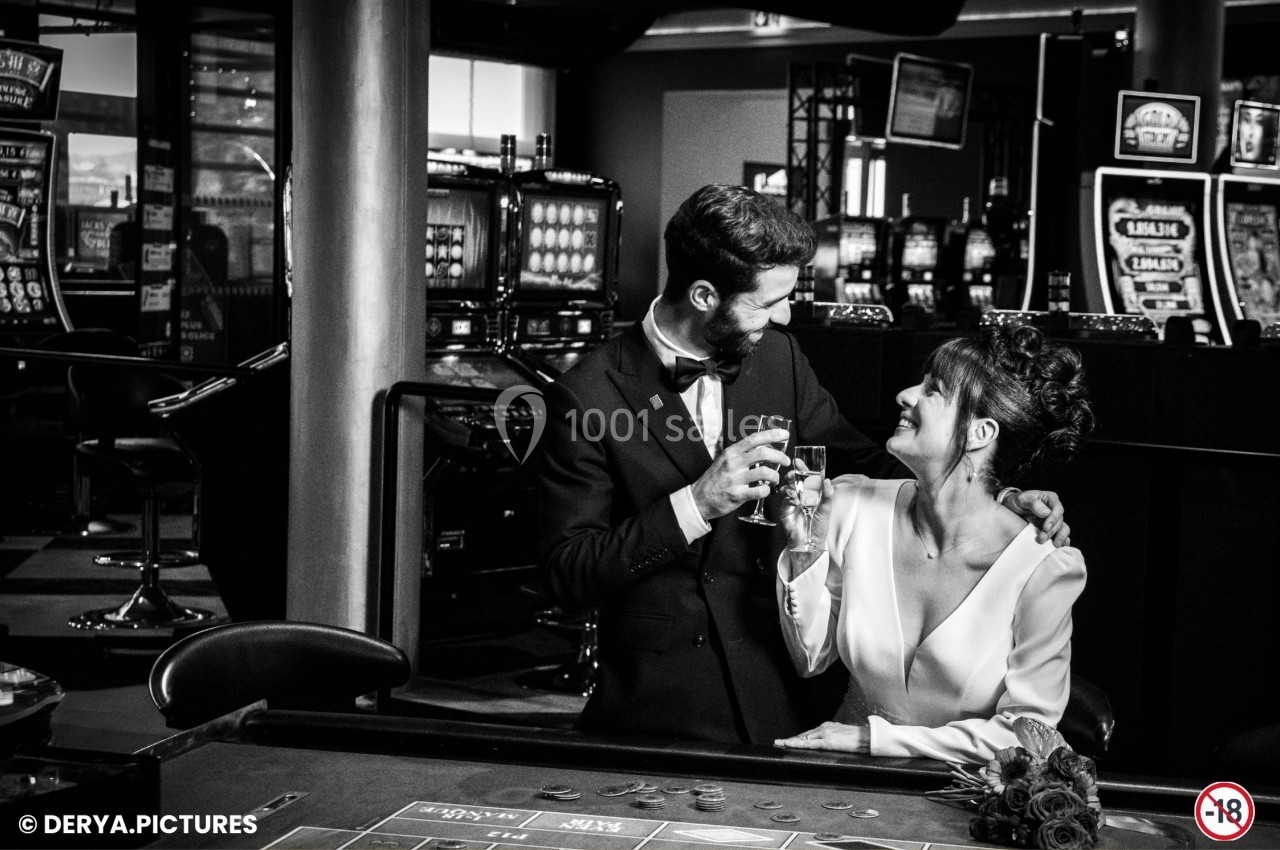 Un couple élégant trinque devant une table de casino, entouré de machines à sous en arrière-plan.