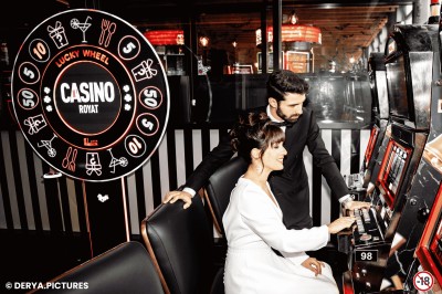 Un couple en tenue de mariage danse au milieu d'une salle de casino entourée de machines à sous.