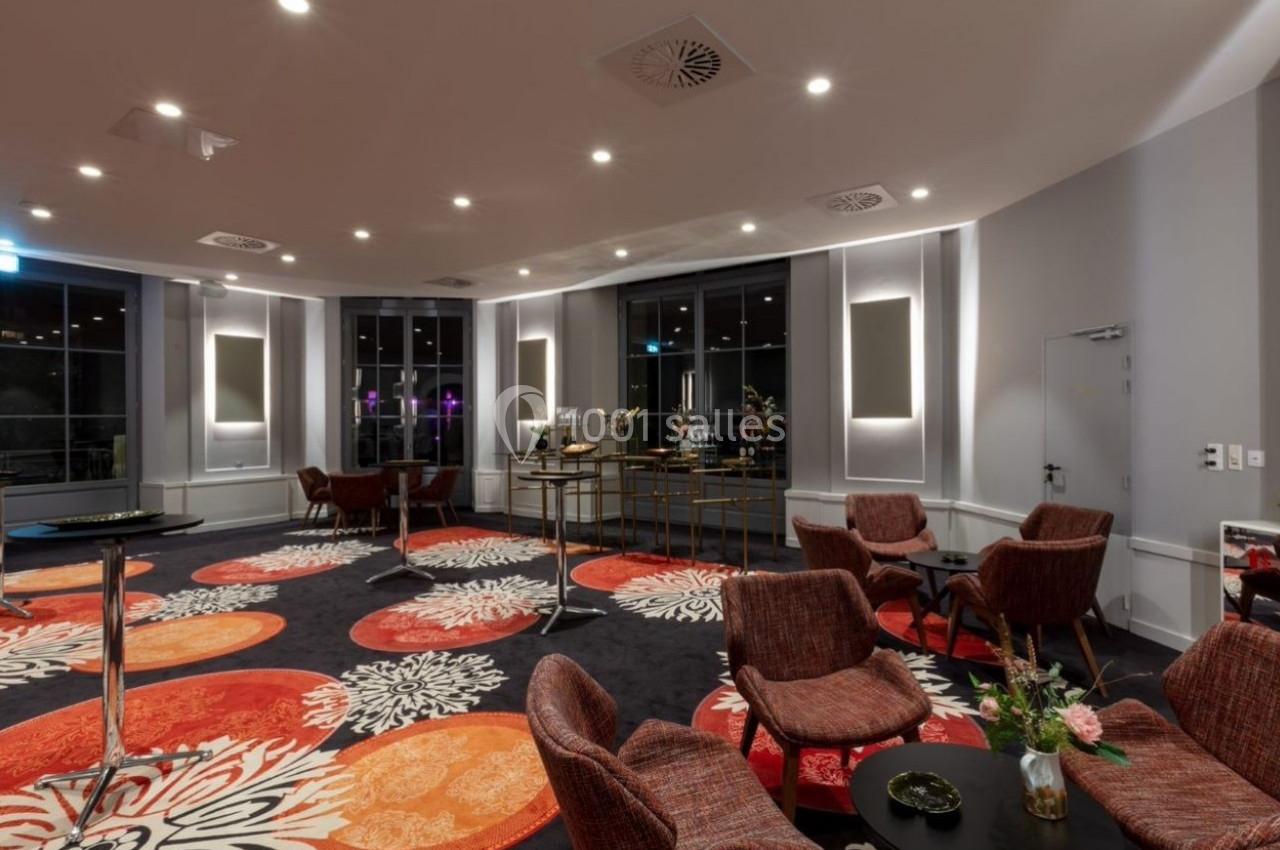 Salle de réception moderne avec moquette colorée, tables hautes, chaises en tissu et éclairage tamisé.