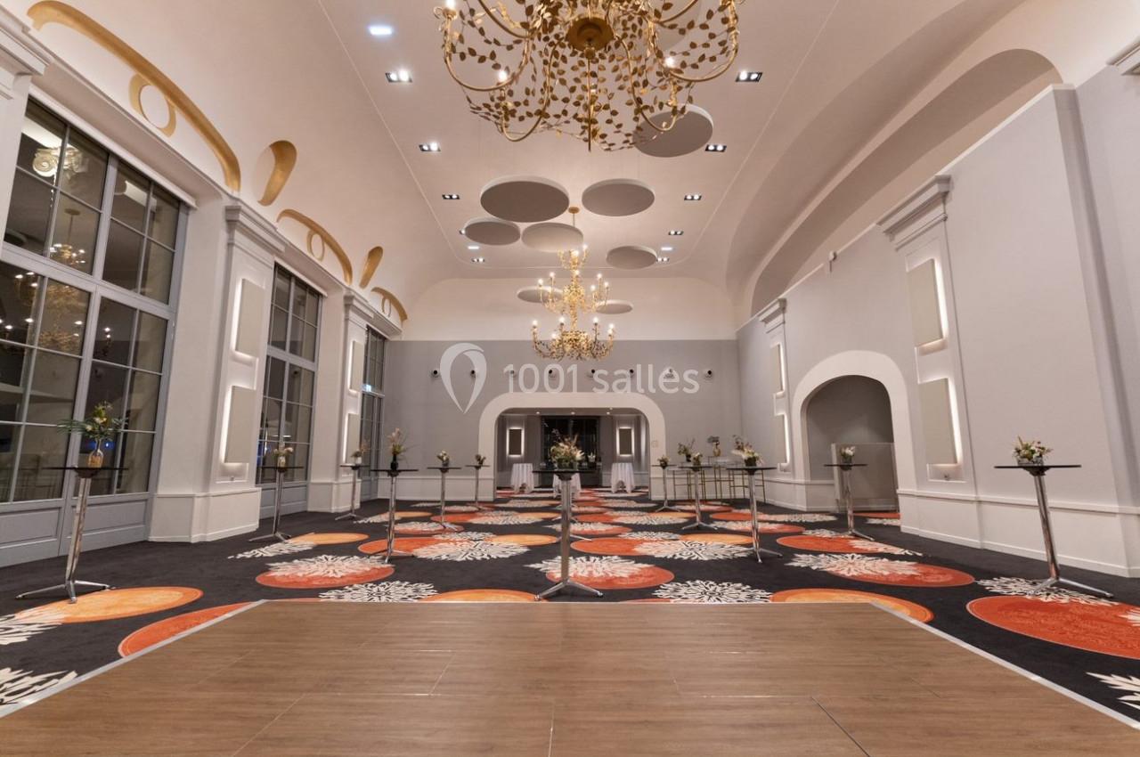 Salle de réception élégante avec lustres dorés, tapis coloré et tables hautes décorées de fleurs.