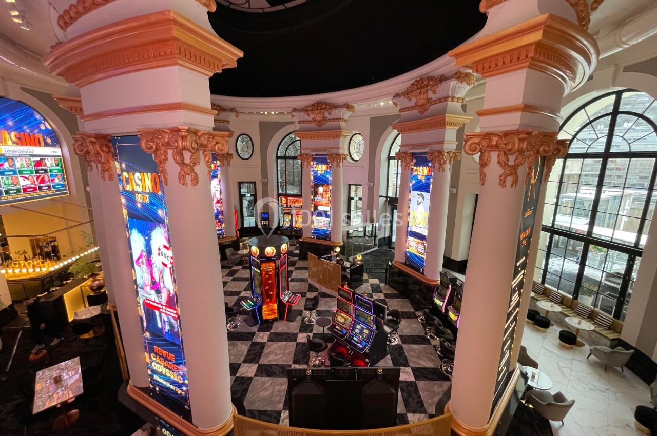 Salle de casino avec machines à sous, colonnes décoratives et éclairage lumineux dans un espace élégant.