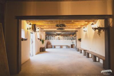 Vue d'une grange en bois entourée d'arbres, avec des bancs disposés en extérieur sur une pelouse.