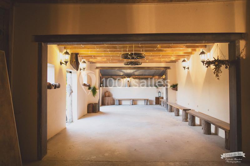 Salle intérieure lumineuse avec murs clairs, bancs en bois, décorations suspendues et toit partiellement en tôle.