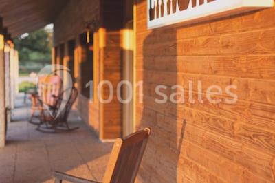 Vue d'une grange en bois entourée d'arbres, avec des bancs disposés en extérieur sur une pelouse.