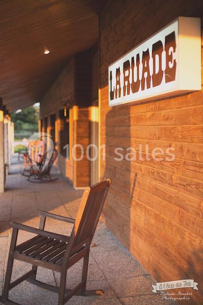Façade en bois d'un bâtiment avec une enseigne ’La Ruade’ et des chaises en bois sur une terrasse ensoleillée.