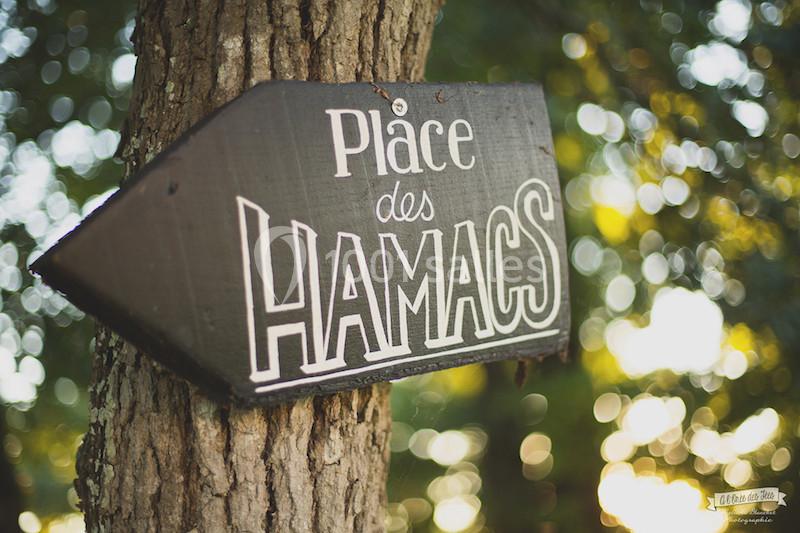 Panneau en bois fixé à un arbre indiquant ’Place des Hamacs’ avec un arrière-plan flou de feuillage.
