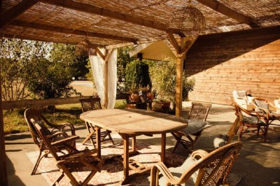 Vue d'une grange en bois entourée d'arbres, avec des bancs disposés en extérieur sur une pelouse.