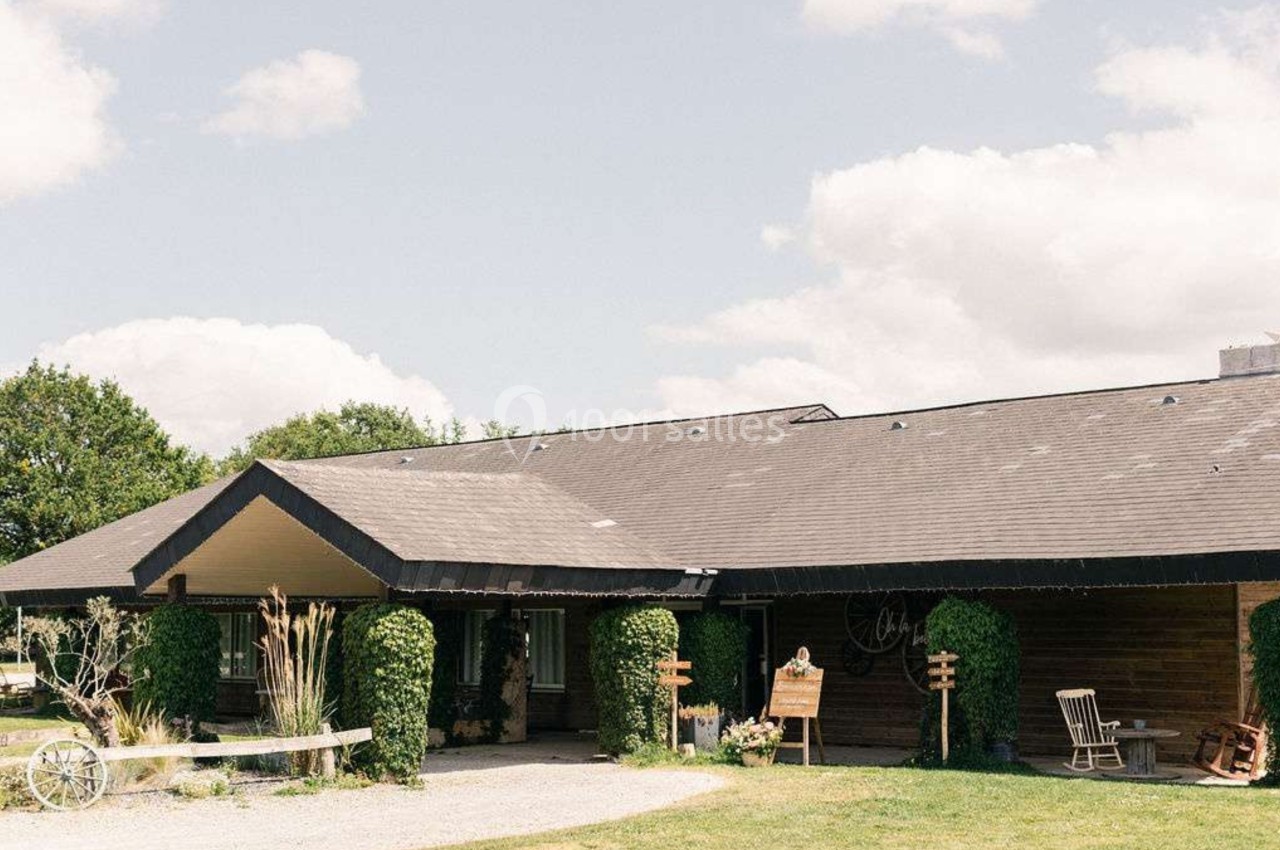 Bâtiment en bois avec toit sombre, entouré de verdure et d'éléments décoratifs extérieurs sous un ciel dégagé.