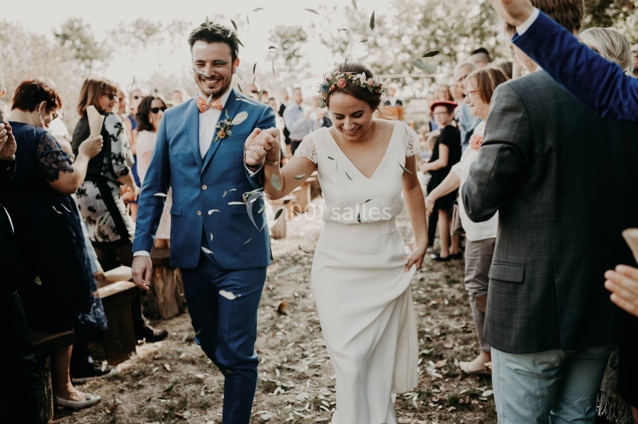Un couple souriant marche main dans la main sous une pluie de pétales lors d'une cérémonie en plein air.