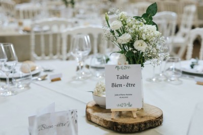 Centre de table avec fleurs séchées dans un bol en céramique et une carte indiquant ’Table Amitié’ sur une rondelle de bois.