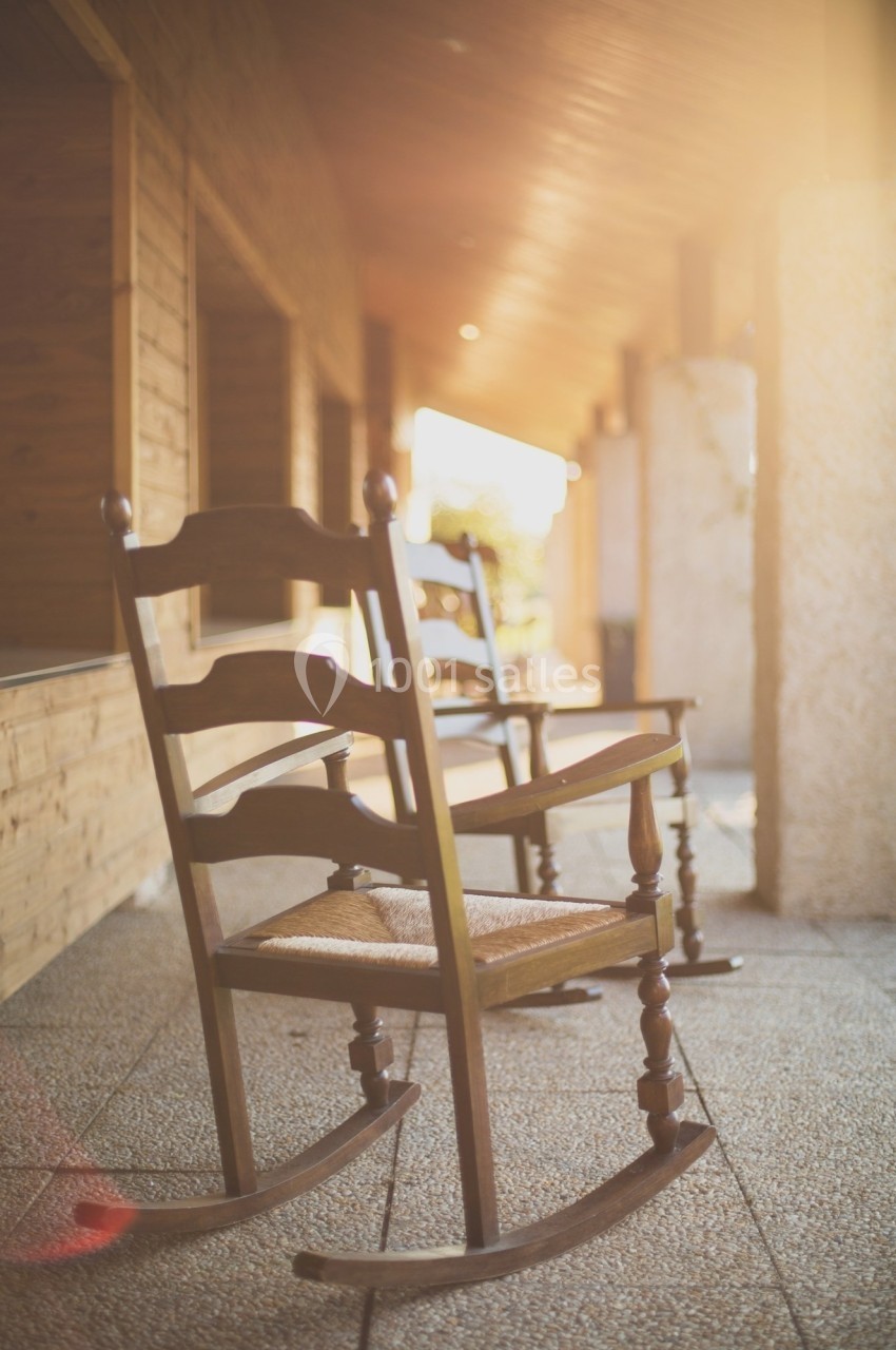 Chaise berçante en bois sur une terrasse ensoleillée avec un sol en pierre et des murs en bois.