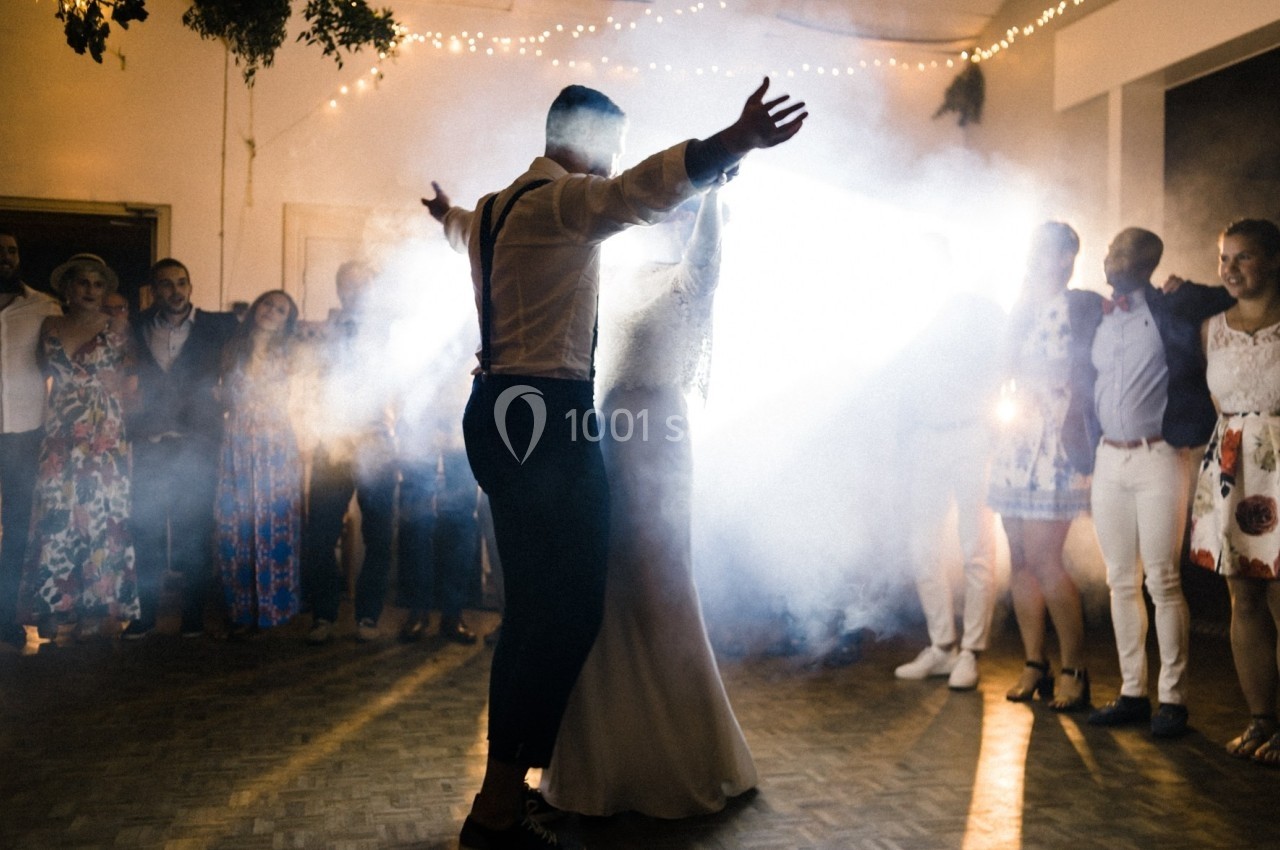 Un couple danse au centre d'une piste entouré d'invités, éclairé par une lumière vive et une légère fumée.