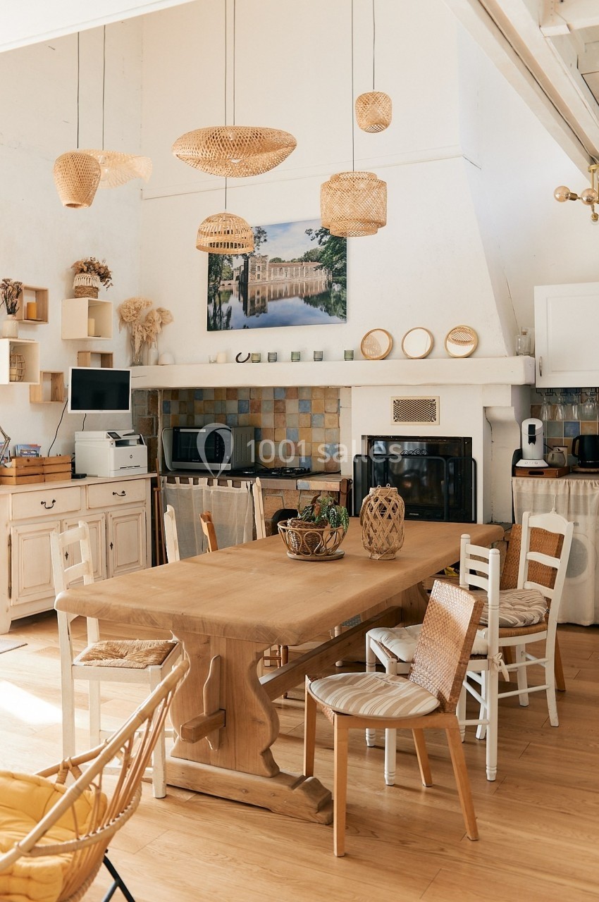 Cuisine lumineuse avec une grande table en bois, chaises assorties et décoration en osier suspendue au plafond.