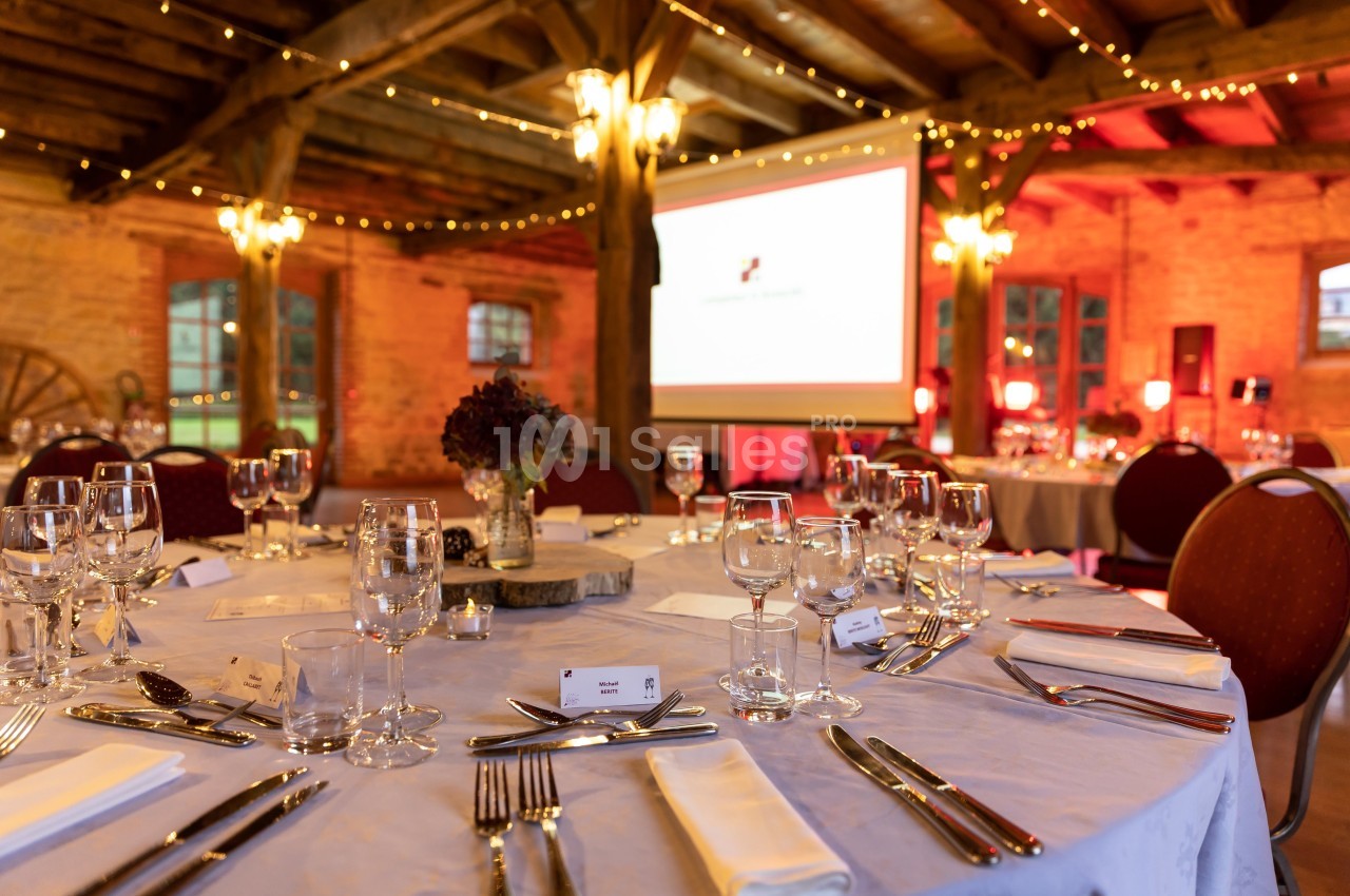Salle de réception décorée avec des tables rondes dressées, éclairage chaleureux et écran de projection en arrière-plan.