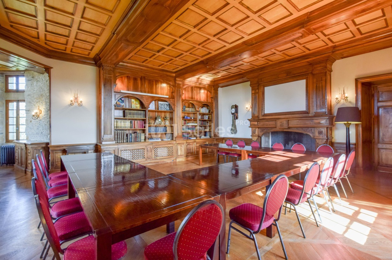 Salle de réunion élégante avec table en bois, chaises rouges, bibliothèque garnie et cheminée dans un décor boisé.