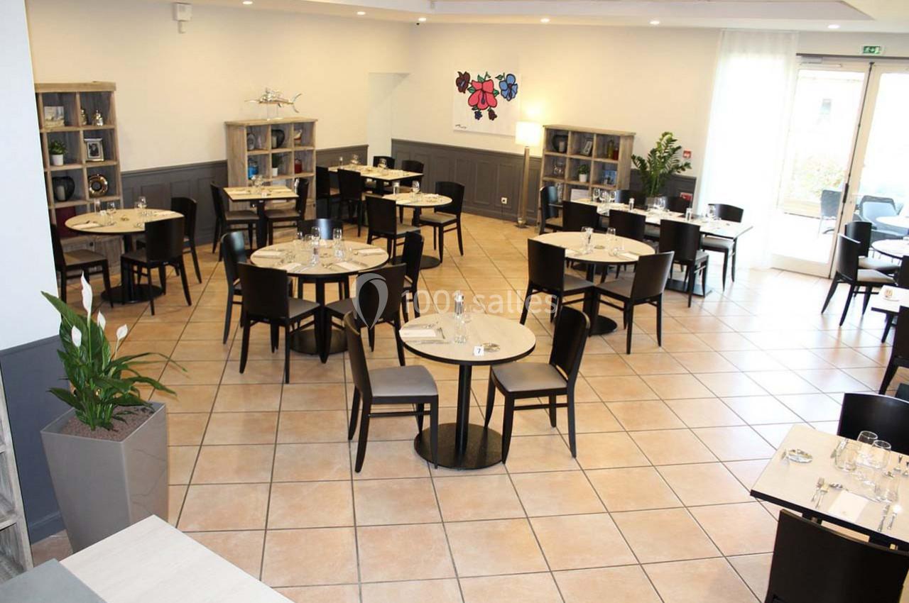 Location salle Les Villages Vovéens (Eure-et-Loir) - Hôtel Restaurant le Quai Fleuri #3 Salle de restaurant lumineuse avec des tables rondes dressées, des chaises noires et des étagères en arrière-plan.