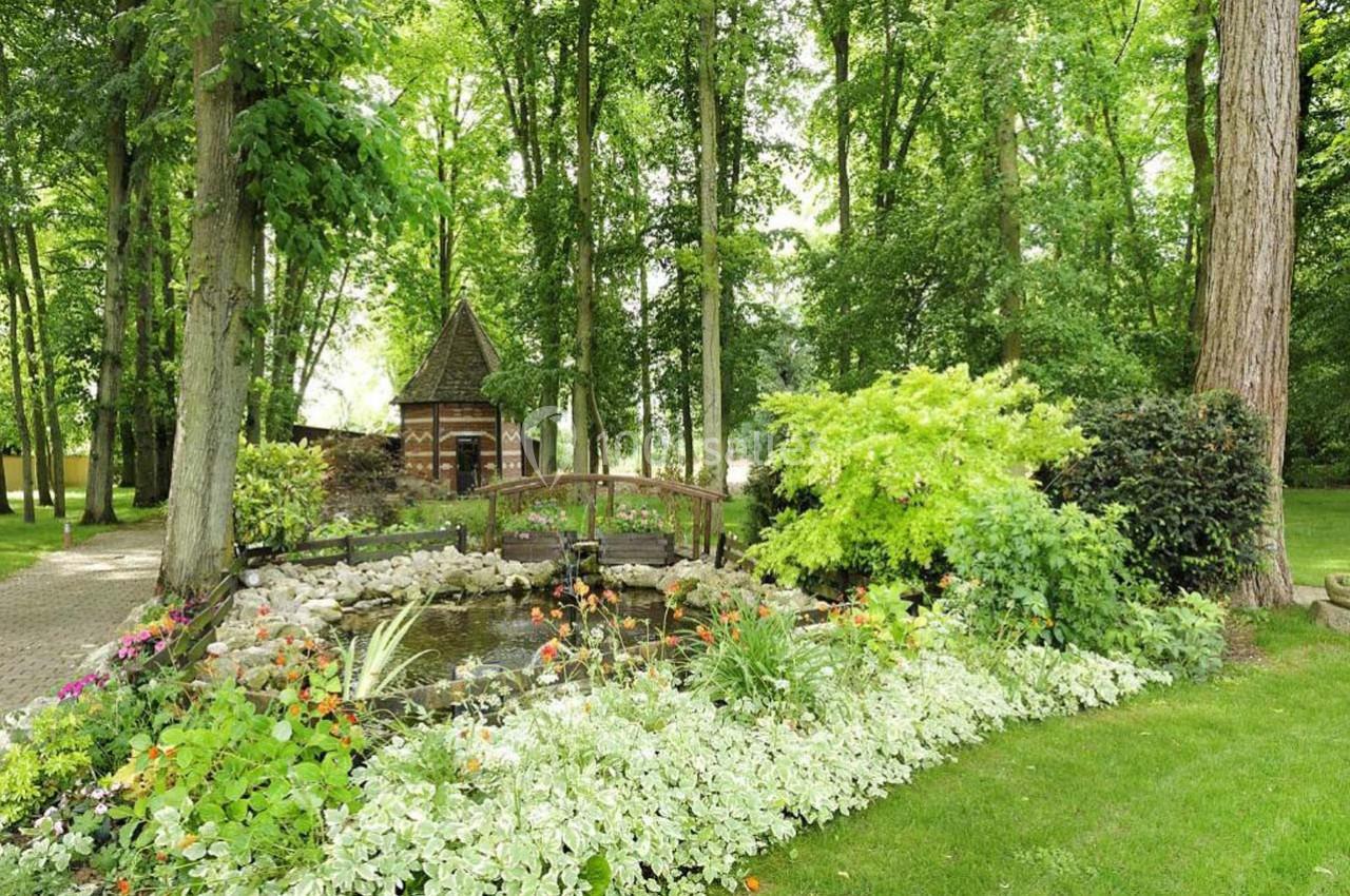 Location salle Les Villages Vovéens (Eure-et-Loir) - Hôtel Restaurant le Quai Fleuri #5 Petit pont en bois surplombant un étang entouré de fleurs et de verdure dans un jardin boisé.