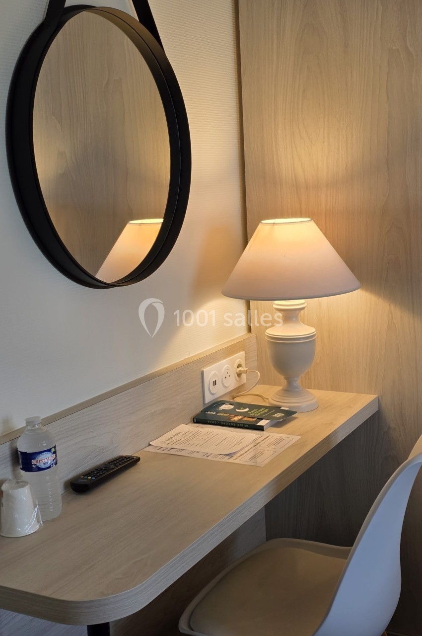 Location salle Les Villages Vovéens (Eure-et-Loir) - Hôtel Restaurant le Quai Fleuri #19 Bureau en bois clair avec une chaise blanche, une lampe allumée, un miroir rond, des documents et une bouteille d'eau.