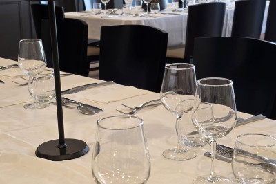 Salle de restaurant lumineuse avec tables dressées, chaises en bois sombre, étagères décoratives et plantes vertes.