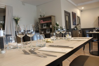 Salle de restaurant lumineuse avec tables dressées, chaises en bois sombre, étagères décoratives et plantes vertes.