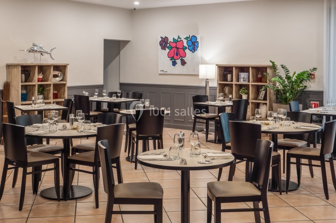 Salle de restaurant lumineuse avec tables dressées, chaises en bois sombre, étagères décoratives et plantes vertes.