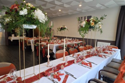 Salle de restaurant lumineuse avec tables dressées, chaises en bois sombre, étagères décoratives et plantes vertes.