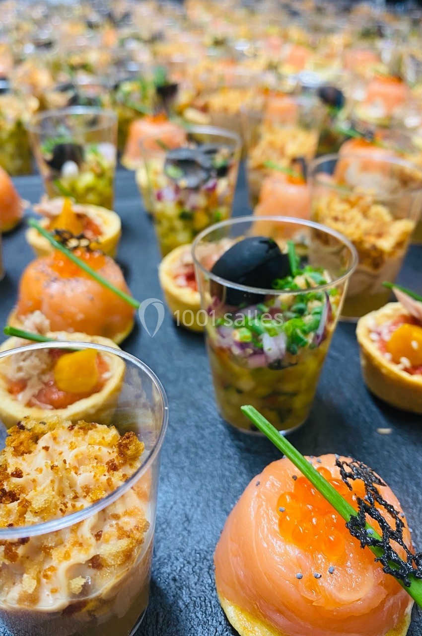 Assortiment de verrines et bouchées apéritives variées disposées sur un plateau noir.