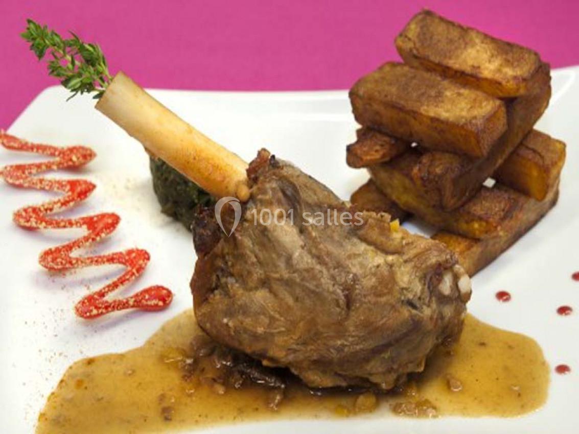 Plat de jarret d'agneau en sauce avec des pommes de terre dorées et une décoration de purée rouge sur une assiette blanche.