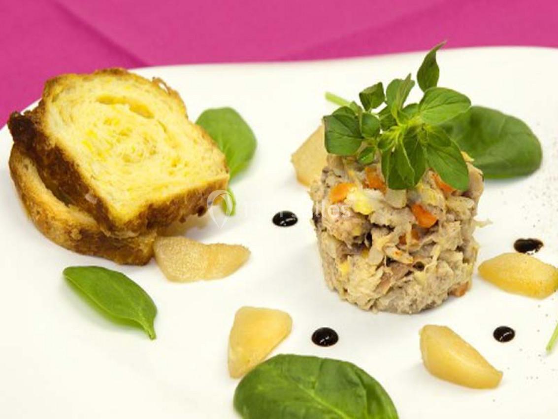 Assiette composée d'un tartare de poisson, de feuilles de mâche, de morceaux de poire et d'une tranche de brioche dorée.