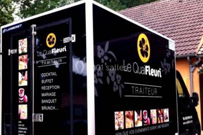 Miniature Traiteur Les Villages Vovéens (Eure-et-Loir) - Le Quai Fleuri #17 Camion noir de traiteur ’Le Quai Fleuri’ garé devant un bâtiment, avec visuels de prestations culinaires sur les panneaux.