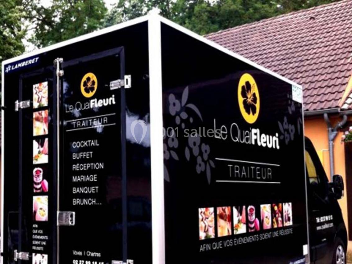 Camion noir de traiteur ’Le Quai Fleuri’ garé devant un bâtiment, avec visuels de prestations culinaires sur les panneaux.