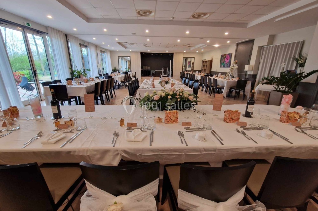 Salle de réception décorée avec des tables dressées, nappes blanches, chaises ornées et centre de table floral.