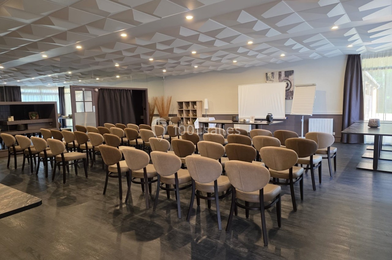 Salle de conférence avec des rangées de chaises alignées, un écran de projection et des étagères en arrière-plan.