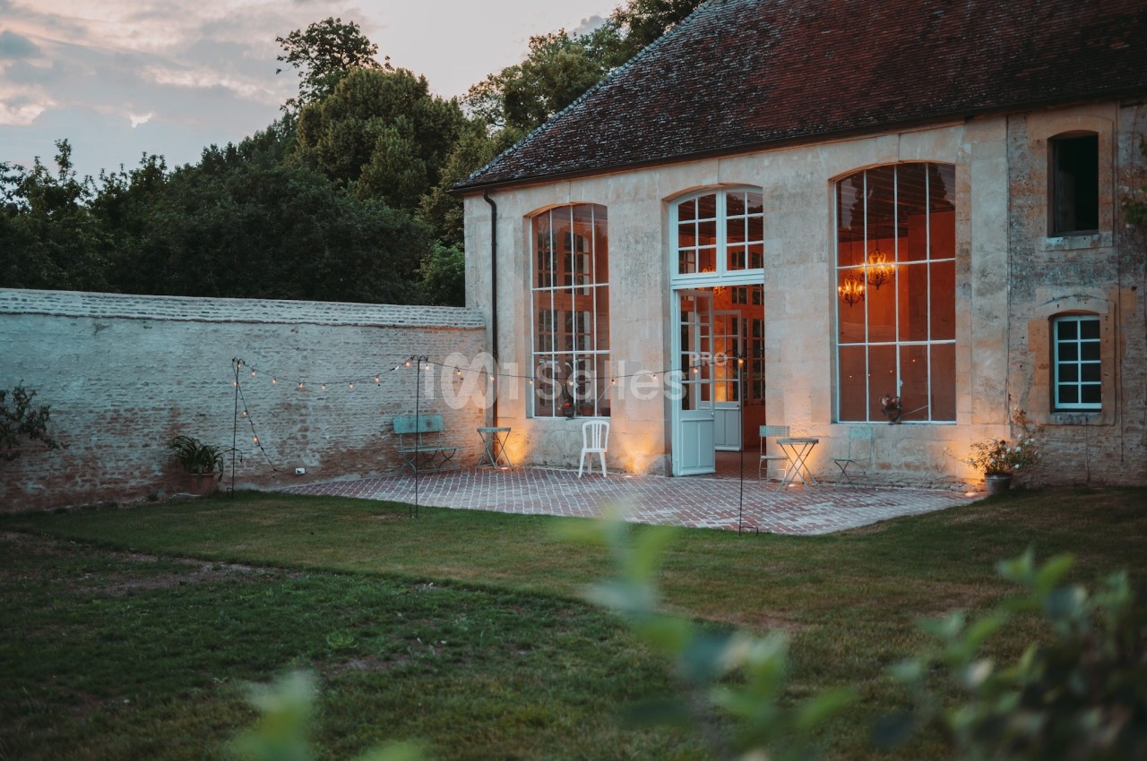Façade d'un bâtiment ancien avec de grandes baies vitrées, éclairé par des guirlandes lumineuses dans un jardin.