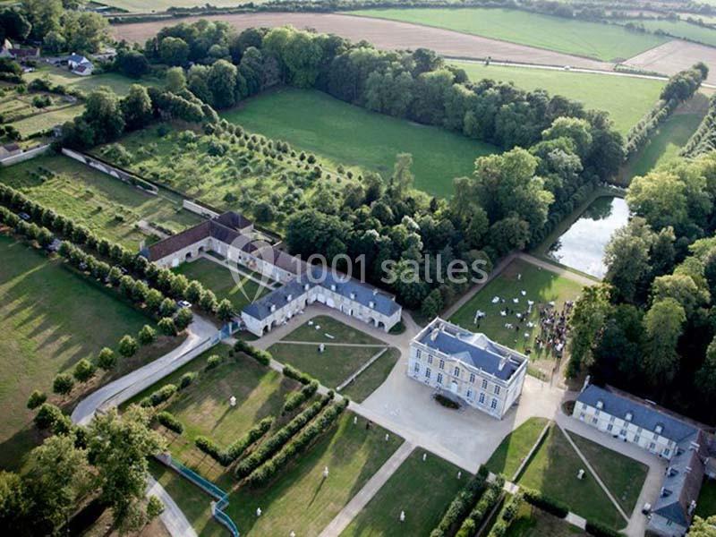 Vue aérienne d'un domaine avec un château, des bâtiments annexes, des jardins aménagés et des champs environnants.