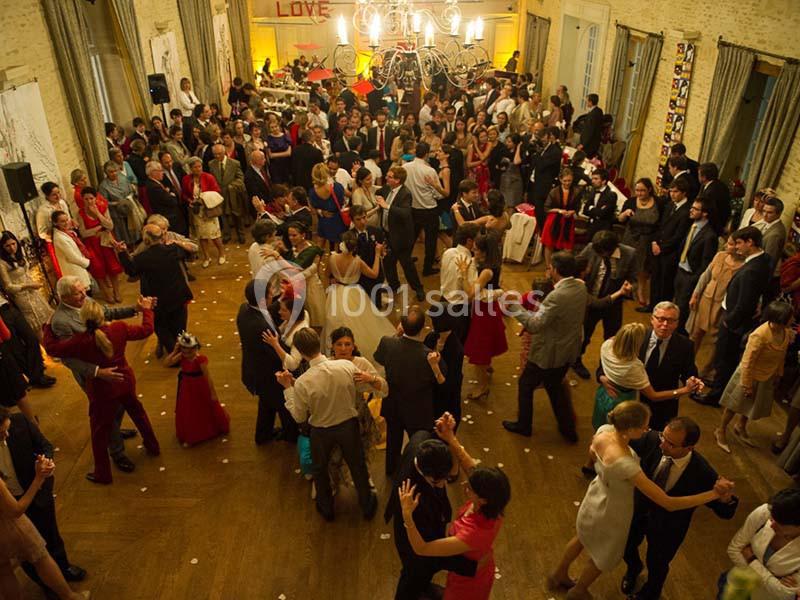 Groupe de personnes dansant dans une salle de réception éclairée, décorée pour un événement festif.