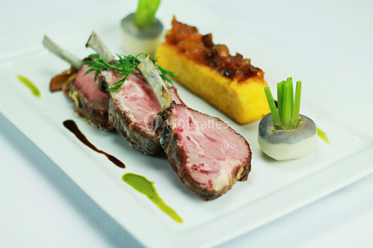 Carré d'agneau rôti avec garniture de légumes, polenta et sauce décorative sur une assiette blanche.