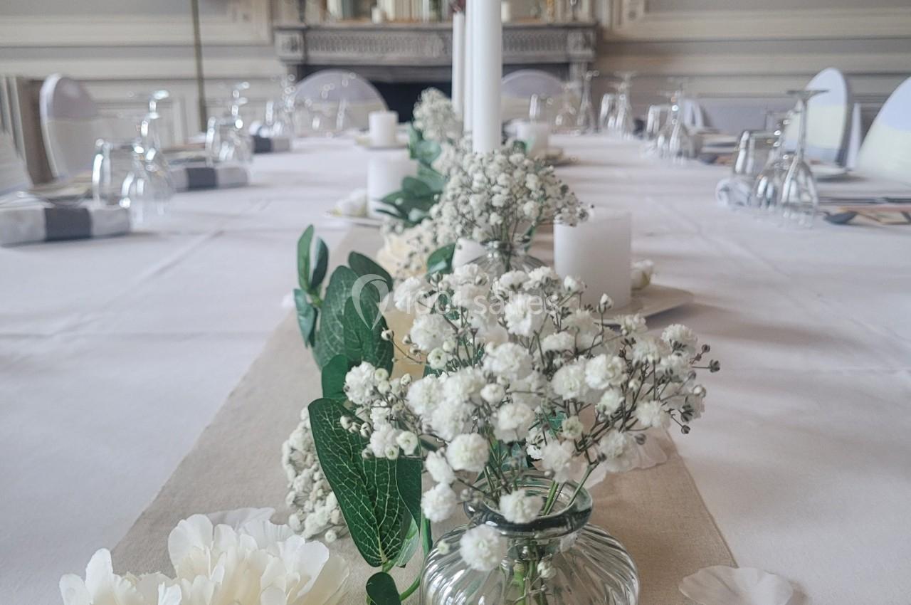 Table décorée avec des fleurs blanches, feuillage et bougies, dans une salle élégante avec miroir et lustre.