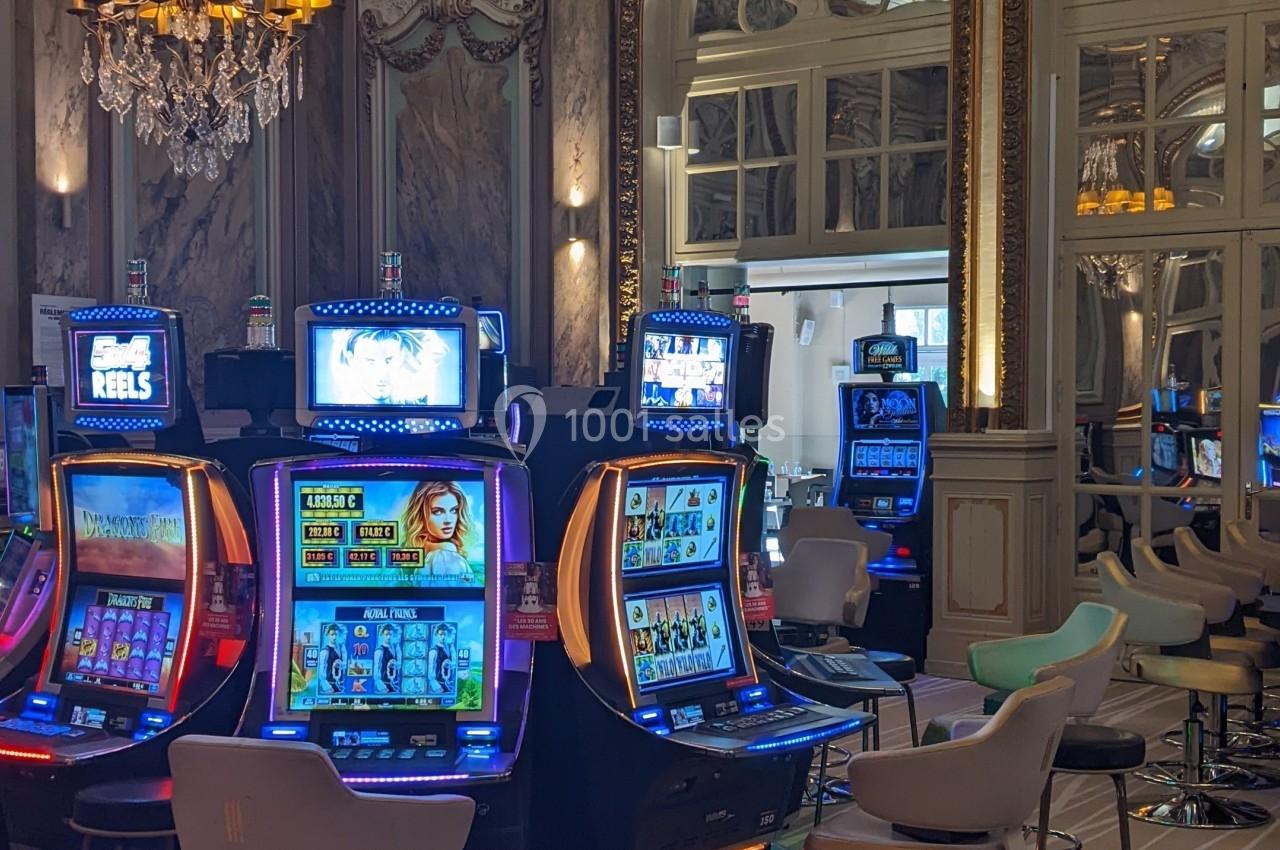 Salle de casino élégante avec machines à sous illuminées, décorations classiques et lustre imposant.
