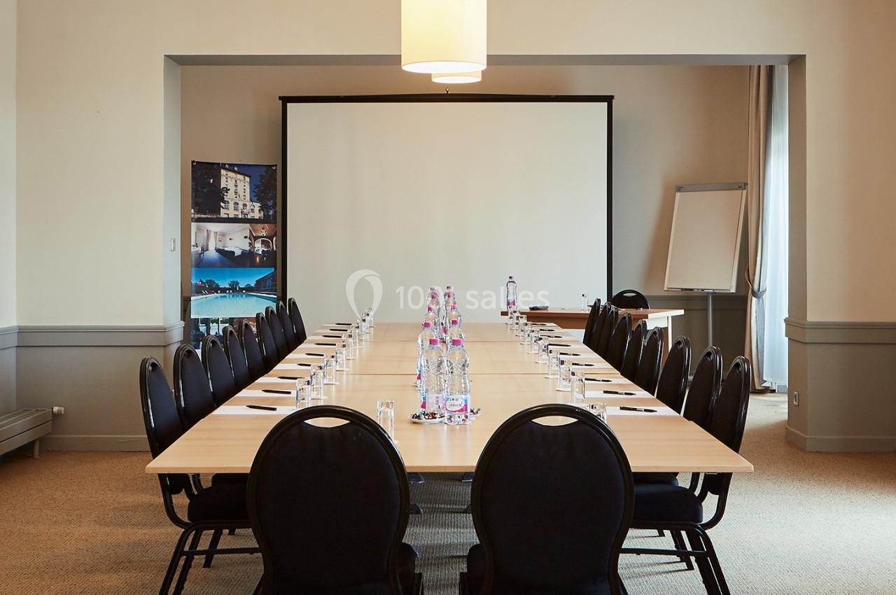 Salle de réunion lumineuse avec une grande table rectangulaire, des chaises noires et un écran de projection.