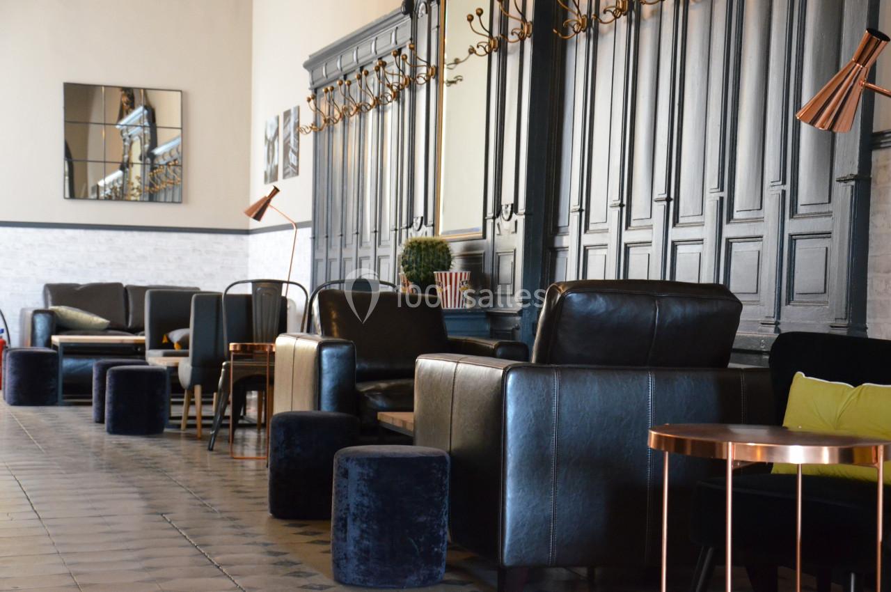 Salle avec fauteuils en cuir noir, tabourets en velours, tables basses et mur en boiseries sombres.