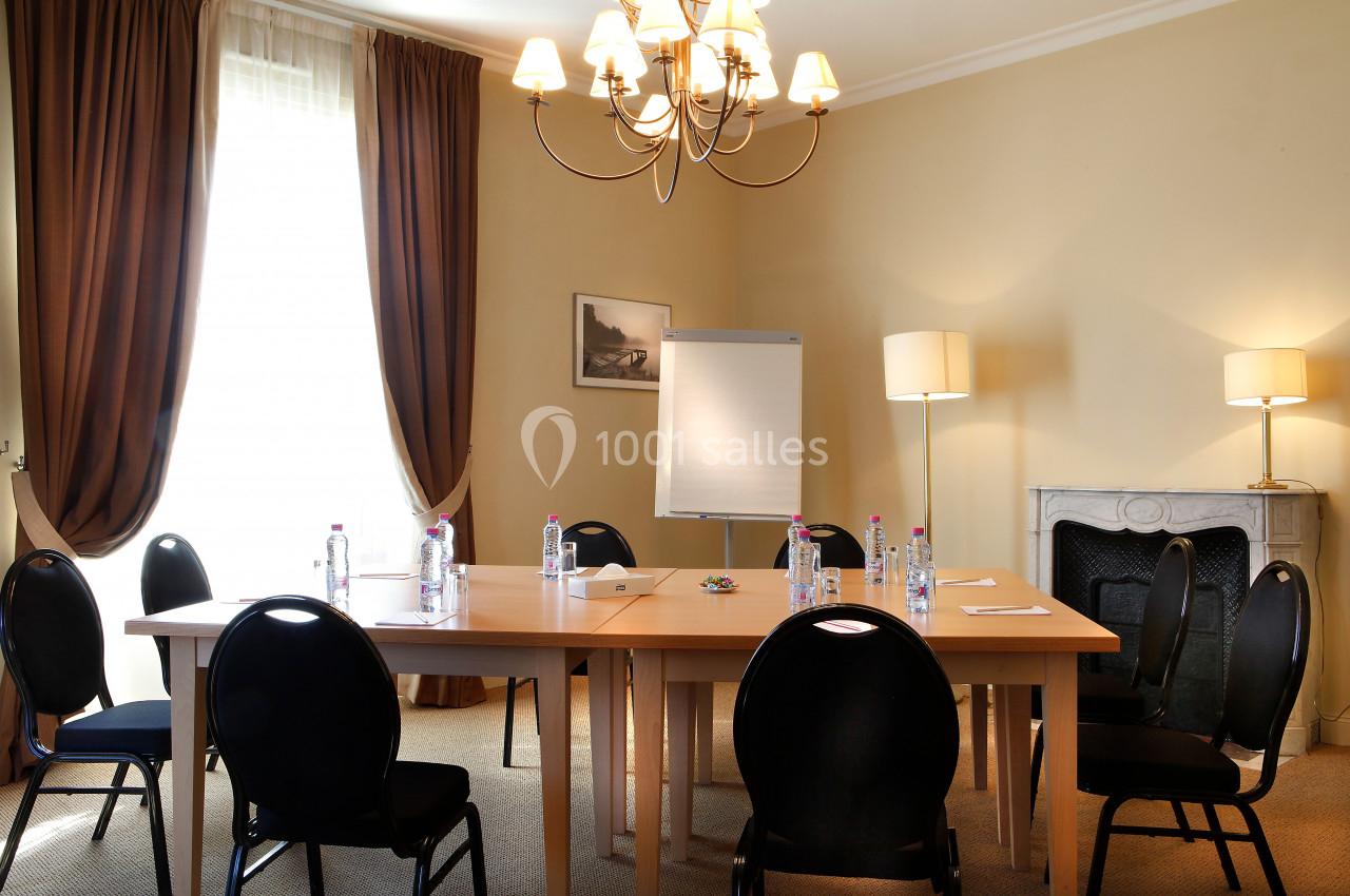 Salle de réunion avec table en bois, chaises noires, paperboard, bouteilles d'eau et éclairage naturel.