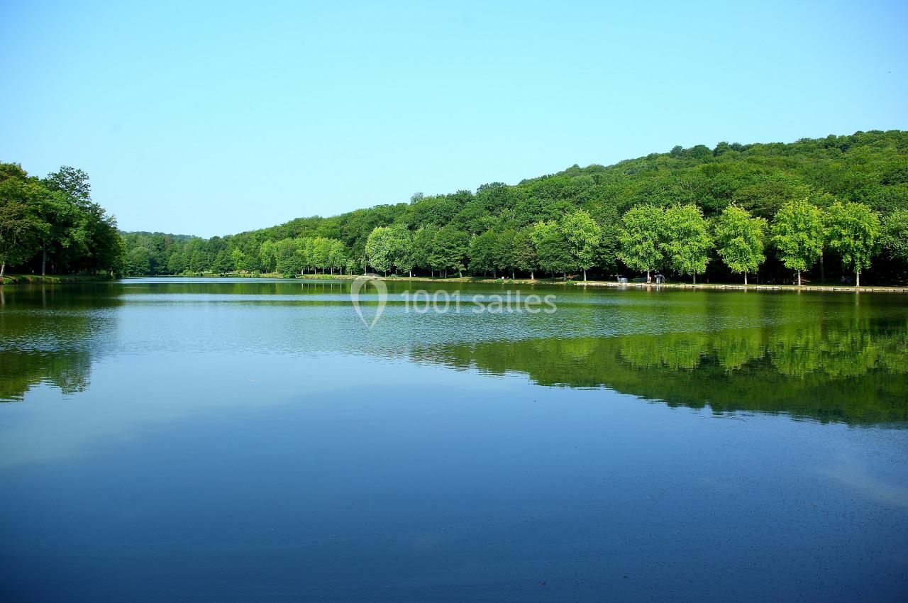 Vue d'un lac calme entouré d'une forêt verdoyante sous un ciel bleu clair.