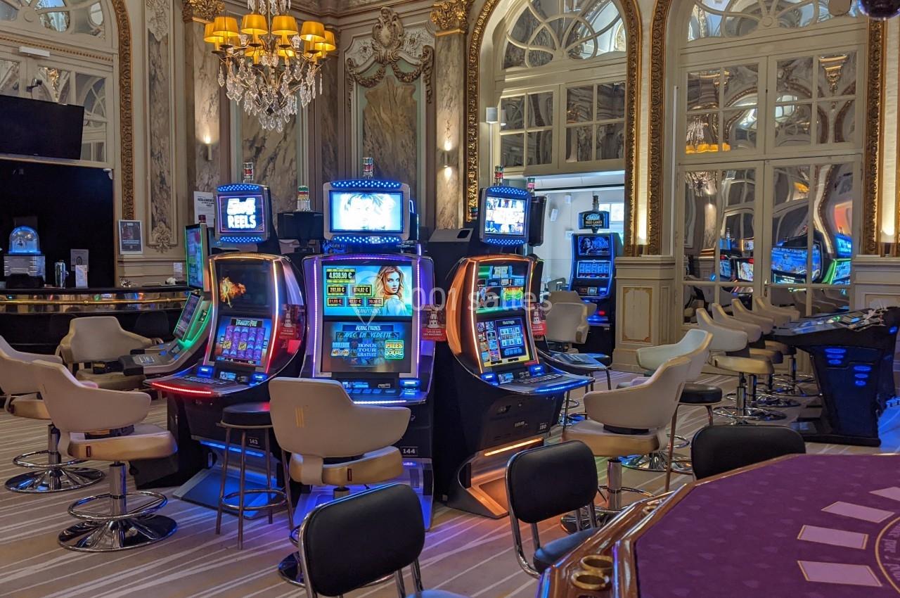 Salle de casino avec machines à sous lumineuses, chaises rembourrées, décorations élégantes et miroirs ornés.
