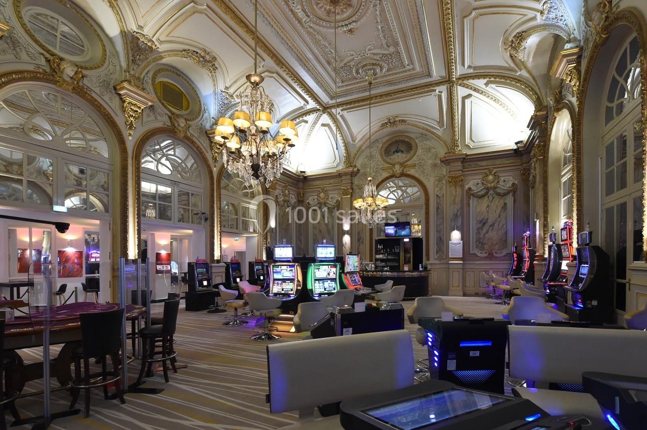 Salle de casino élégante avec machines à sous, tables de jeu, lustres et décorations intérieures ornées.