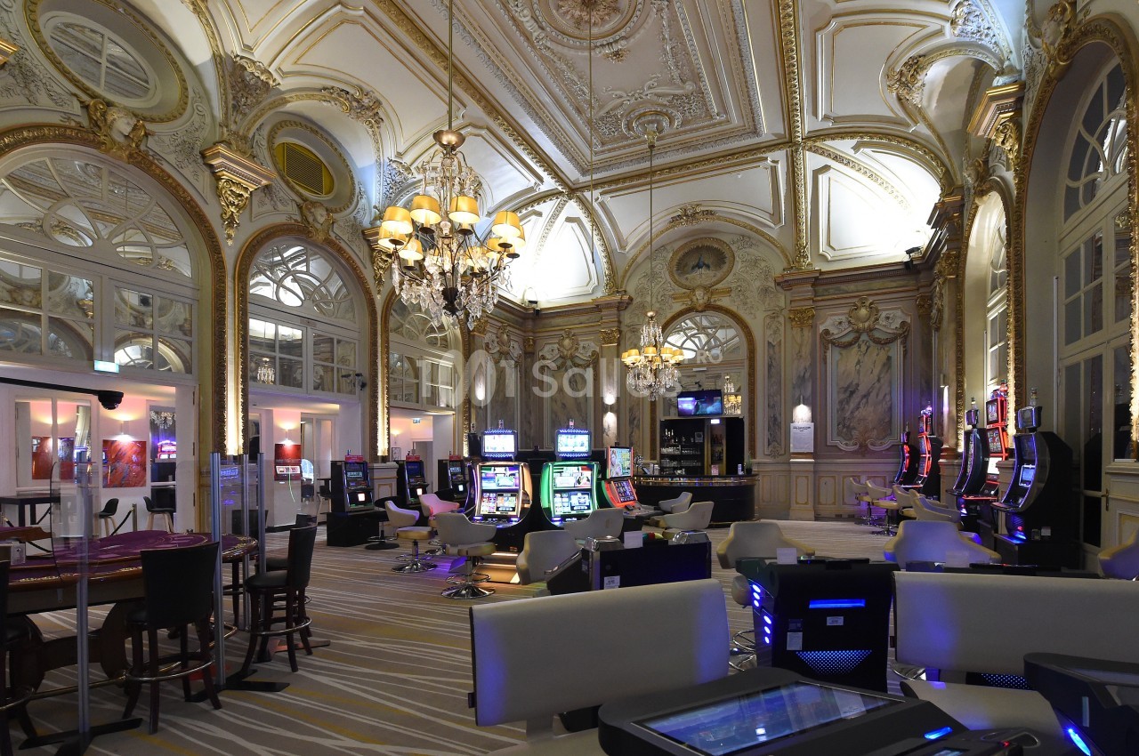 Salle de casino élégante avec machines à sous, tables de jeu, lustres et décorations intérieures ornées.