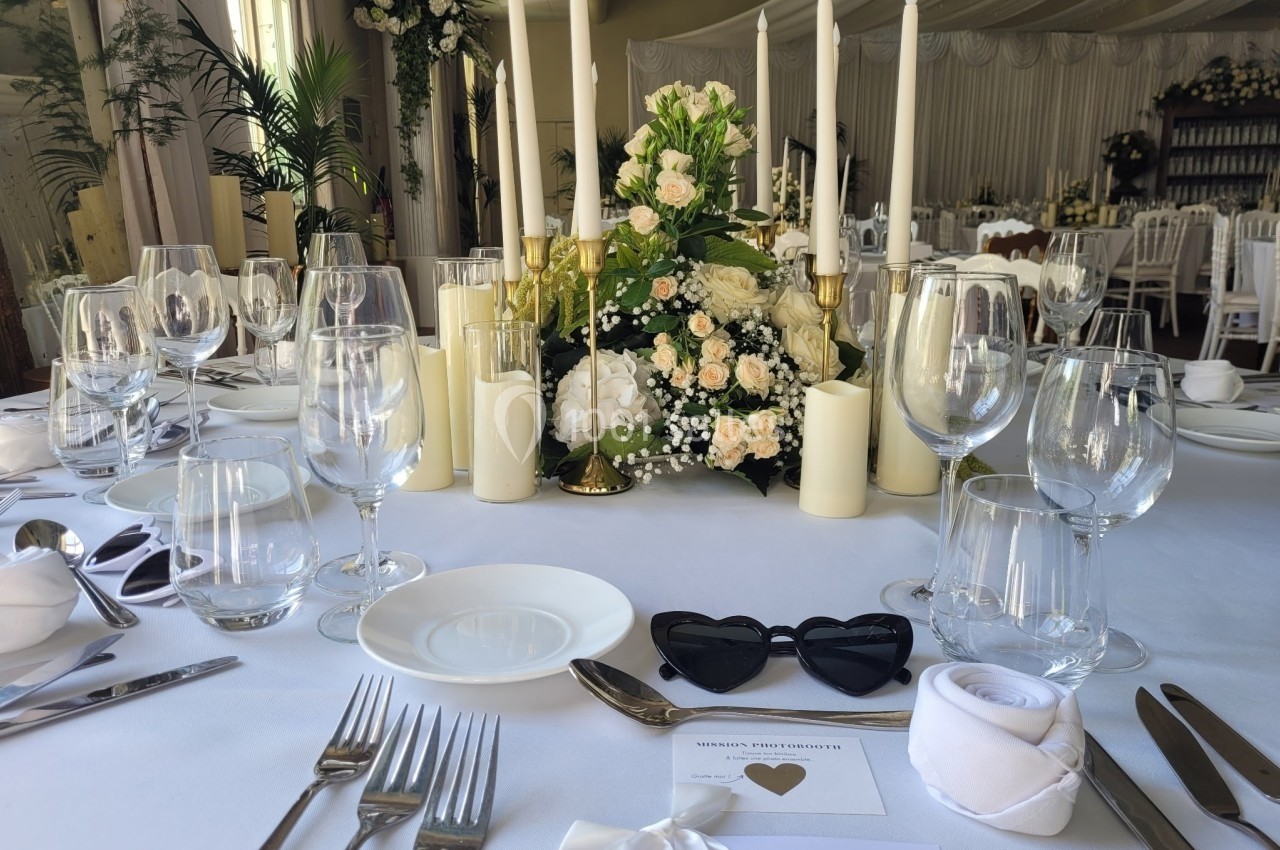 Table élégamment dressée avec des chandeliers, des fleurs blanches et des verres, dans une salle de réception décorée.