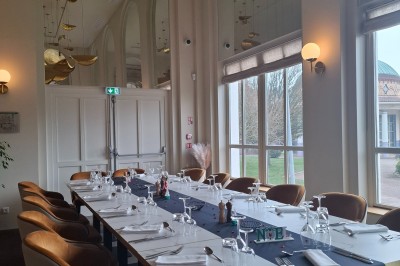 Tasse de café sur une table avec un macaron vert et un plateau de desserts flous en arrière-plan.